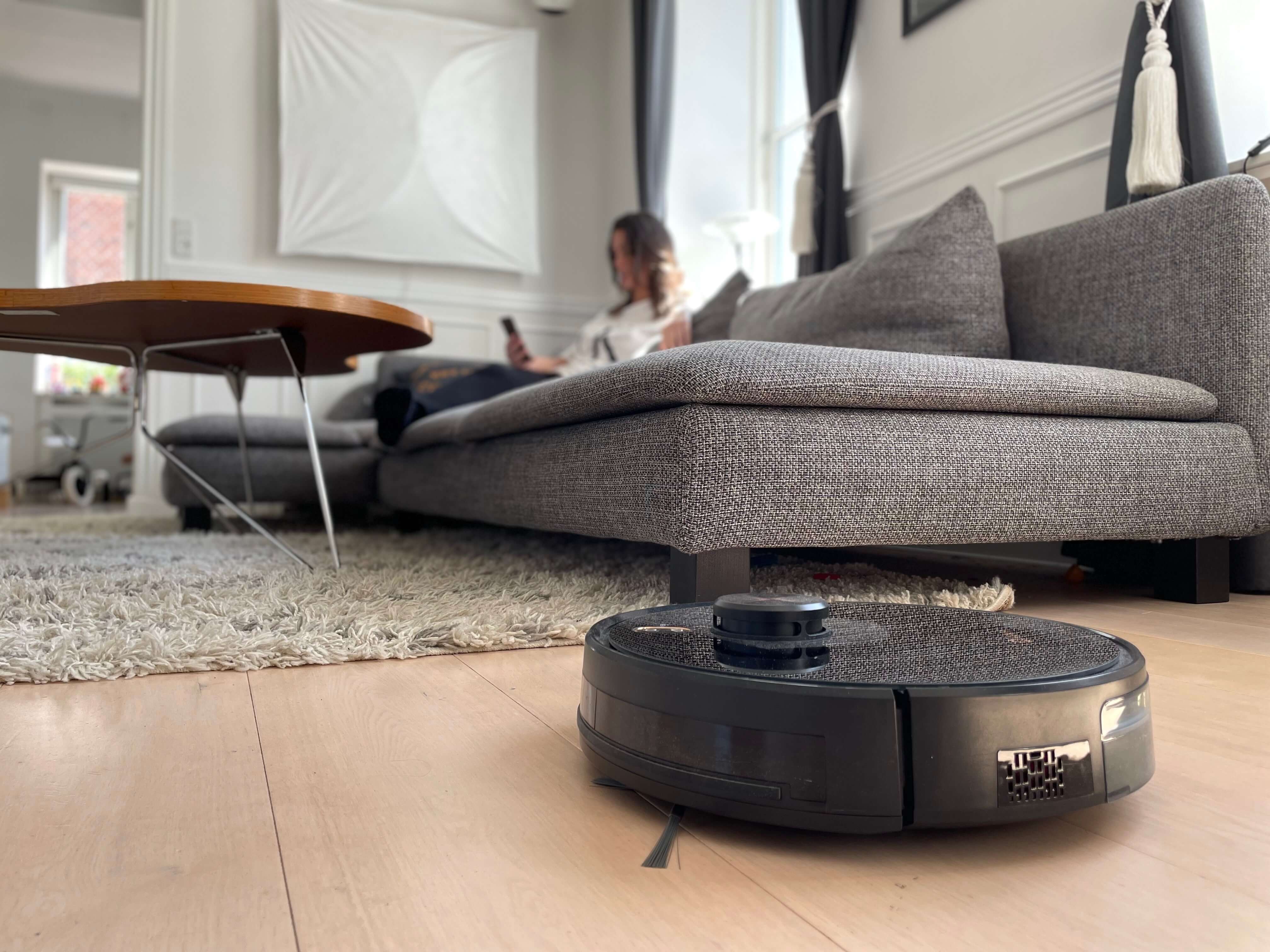 Robotstøvsuger støvsuger stuegulv mens kvinde på sofa slapper af